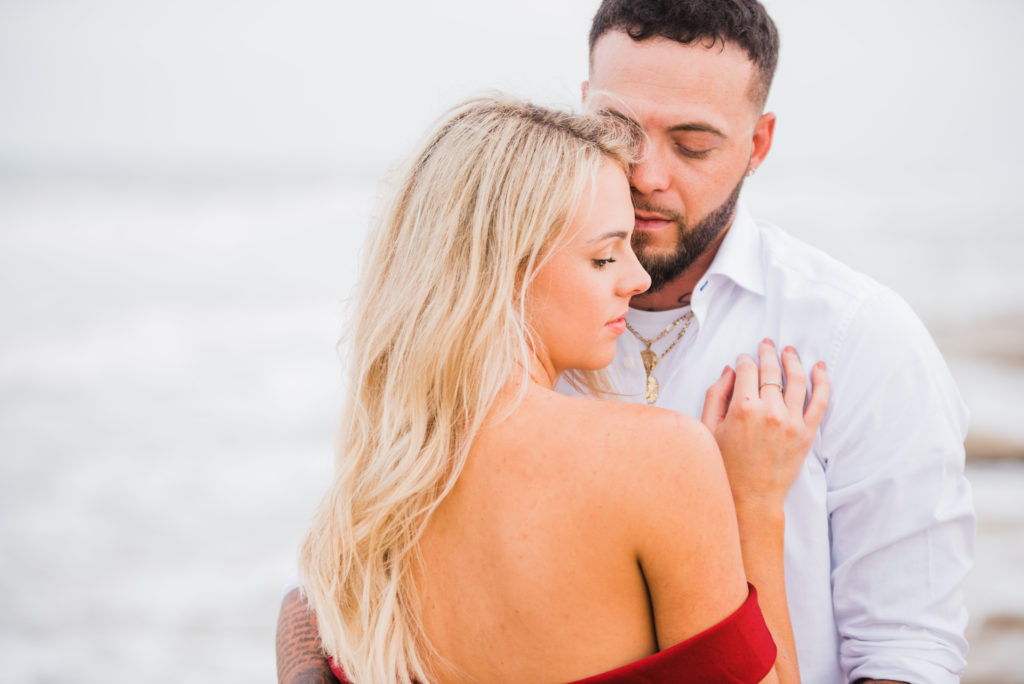 bride wears a red off the shoulder dress and the couple hugs and enjoys a moment together on the beach in palm coast
photo by Chabeli Woolsey of Black Tie & Co www.btcweddings.com